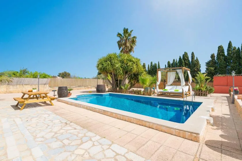 Una piscina al aire libre está junto a un patio pavimentado con asientos y vegetación.