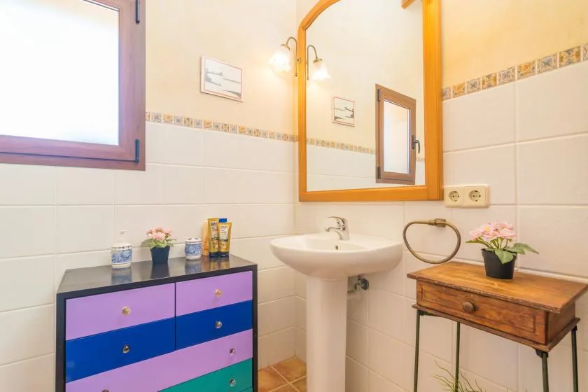 Un baño alicatado con lavabo de pedestal, espejo de pared y armario de colores.