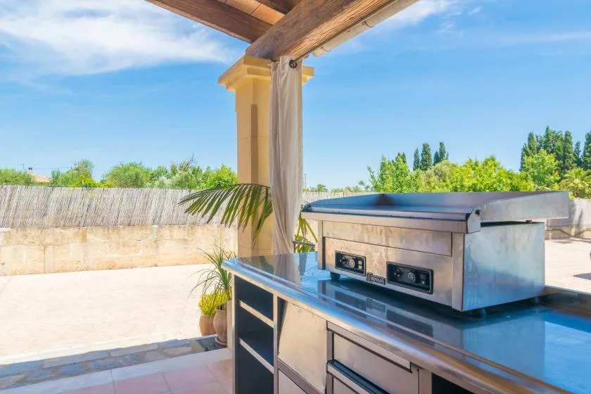 Una encimera de cocina exterior con una parrilla integrada está bajo una pérgola de madera.