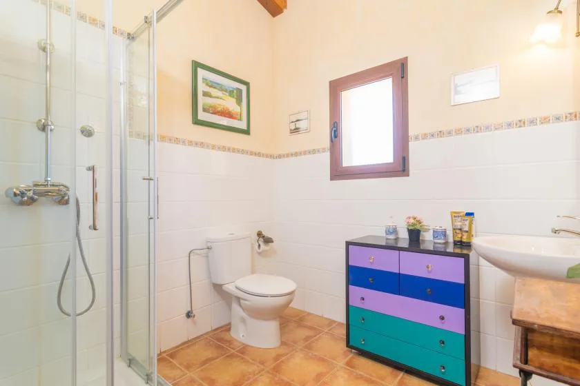 Un baño luminoso con ducha de vidrio, inodoro, lavabo y un mueble colorido.