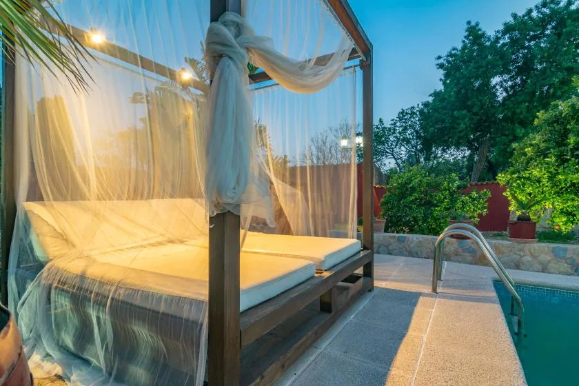 Una cama al aire libre con cortinas translúcidas está junto a una piscina.