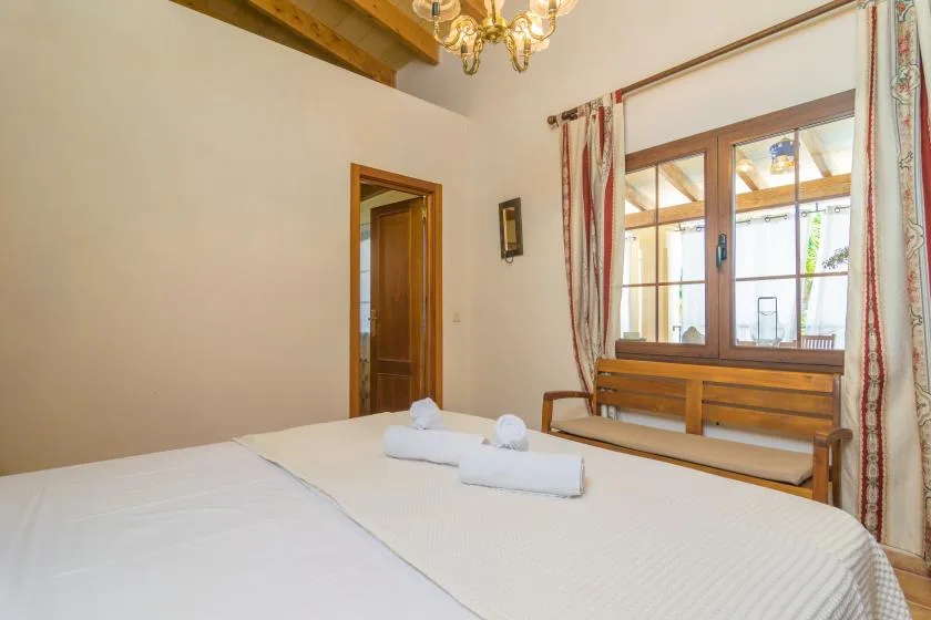 Un dormitorio con una cama bien tendida y un banco de madera bajo la ventana.