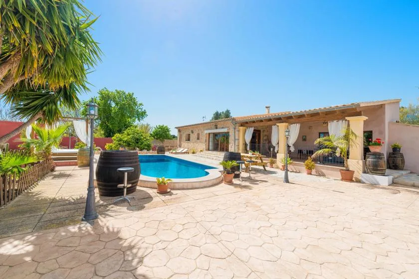Una piscina exterior y un patio pavimentado están junto a un edificio cubierto.