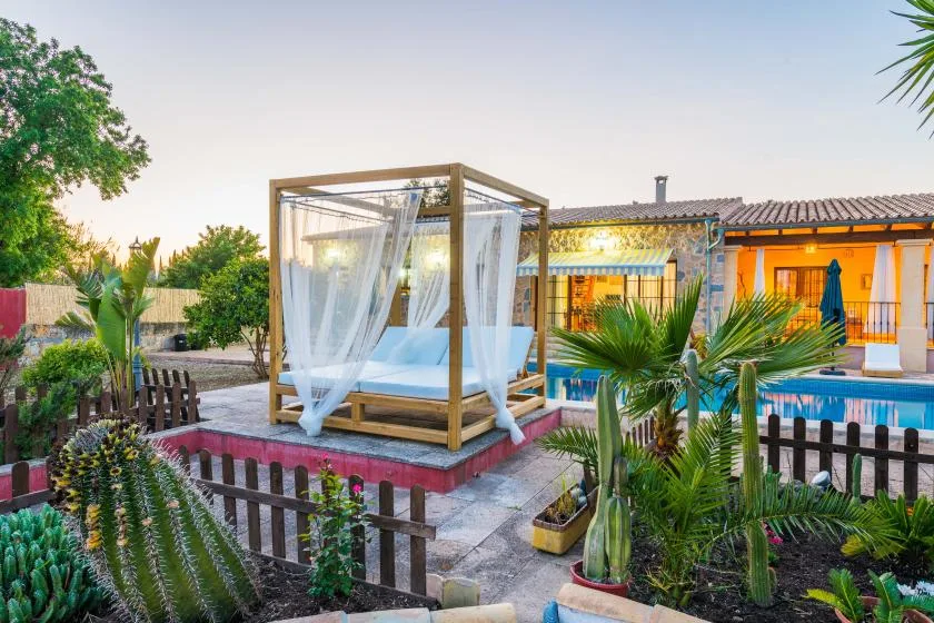 Una zona de piscina al aire libre tiene una cama con cortinas junto al agua.