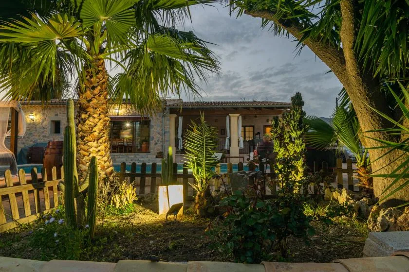 Un jardín con palmeras y un edificio bajo detrás de una cerca de madera.