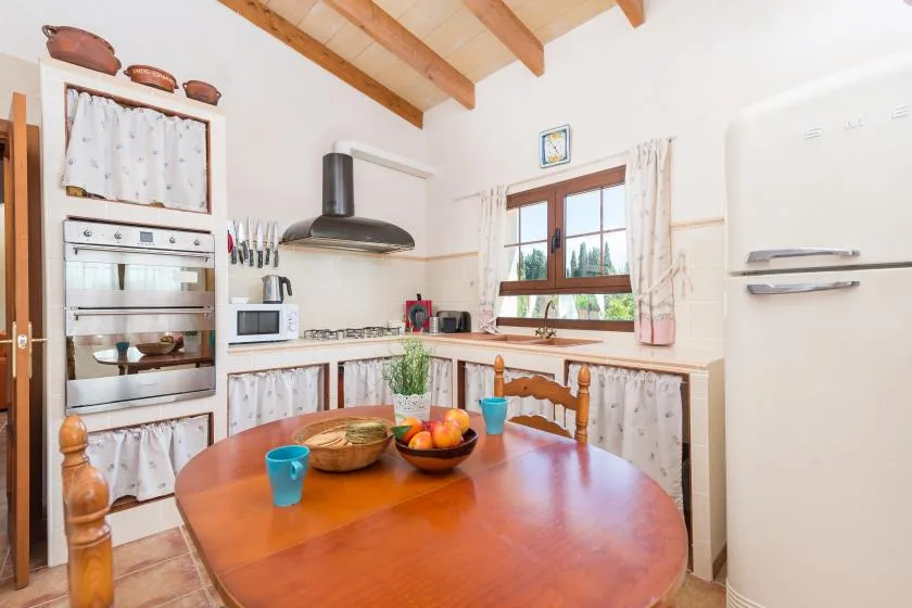 Una cocina luminosa con comedor y una mesa de madera bajo un techo de vigas.