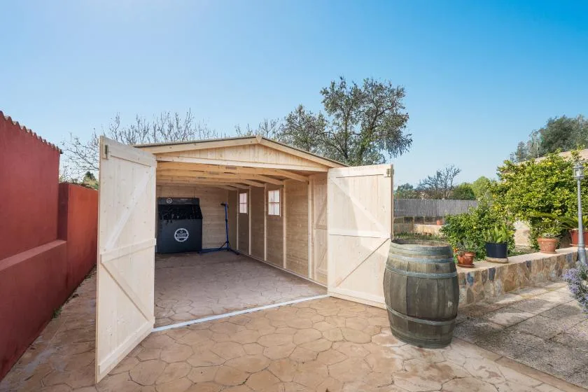 Un garaje de madera abierto está junto a un patio pavimentado con plantas en macetas.