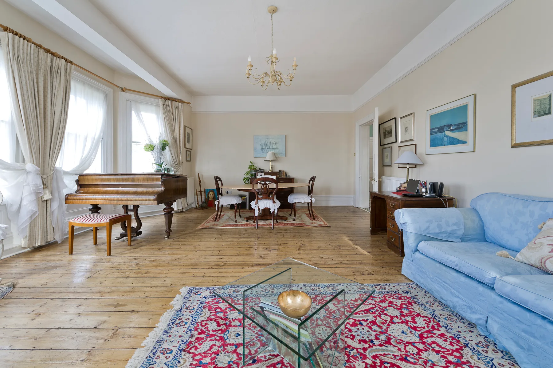 Una sala luminosa con asientos azules, un piano y una mesa de comedor.
