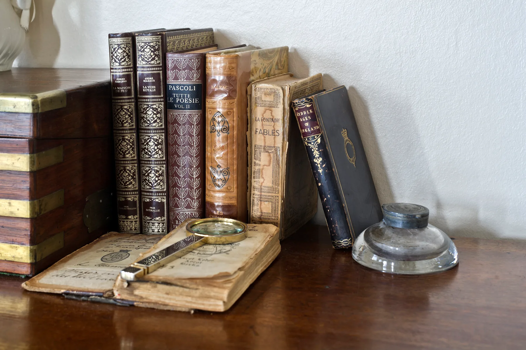 Una mesa muestra libros antiguos, un volumen abierto y un tintero de vidrio.