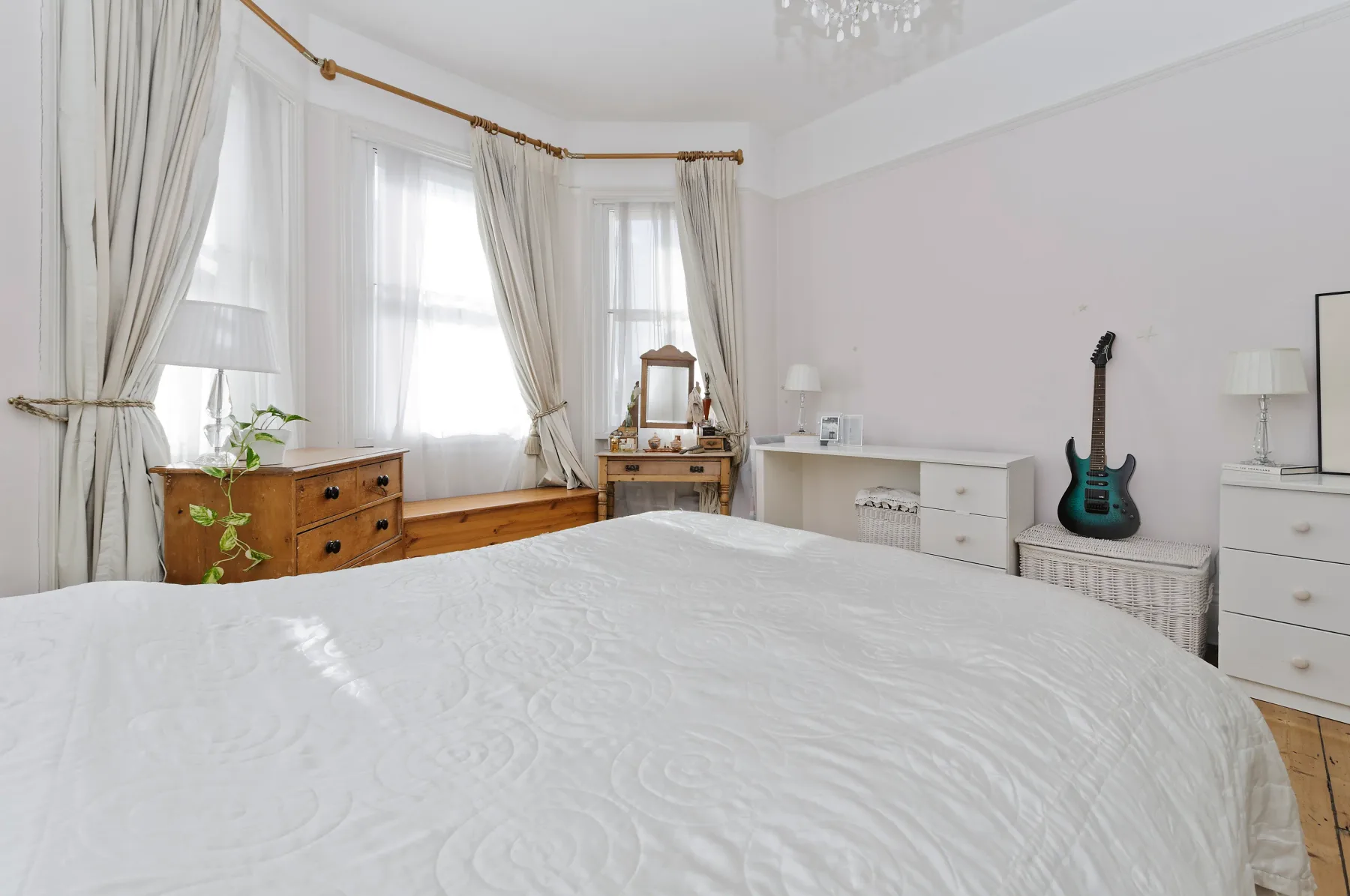Un dormitorio luminoso con una cama grande, ventanas con cortinas y una guitarra.