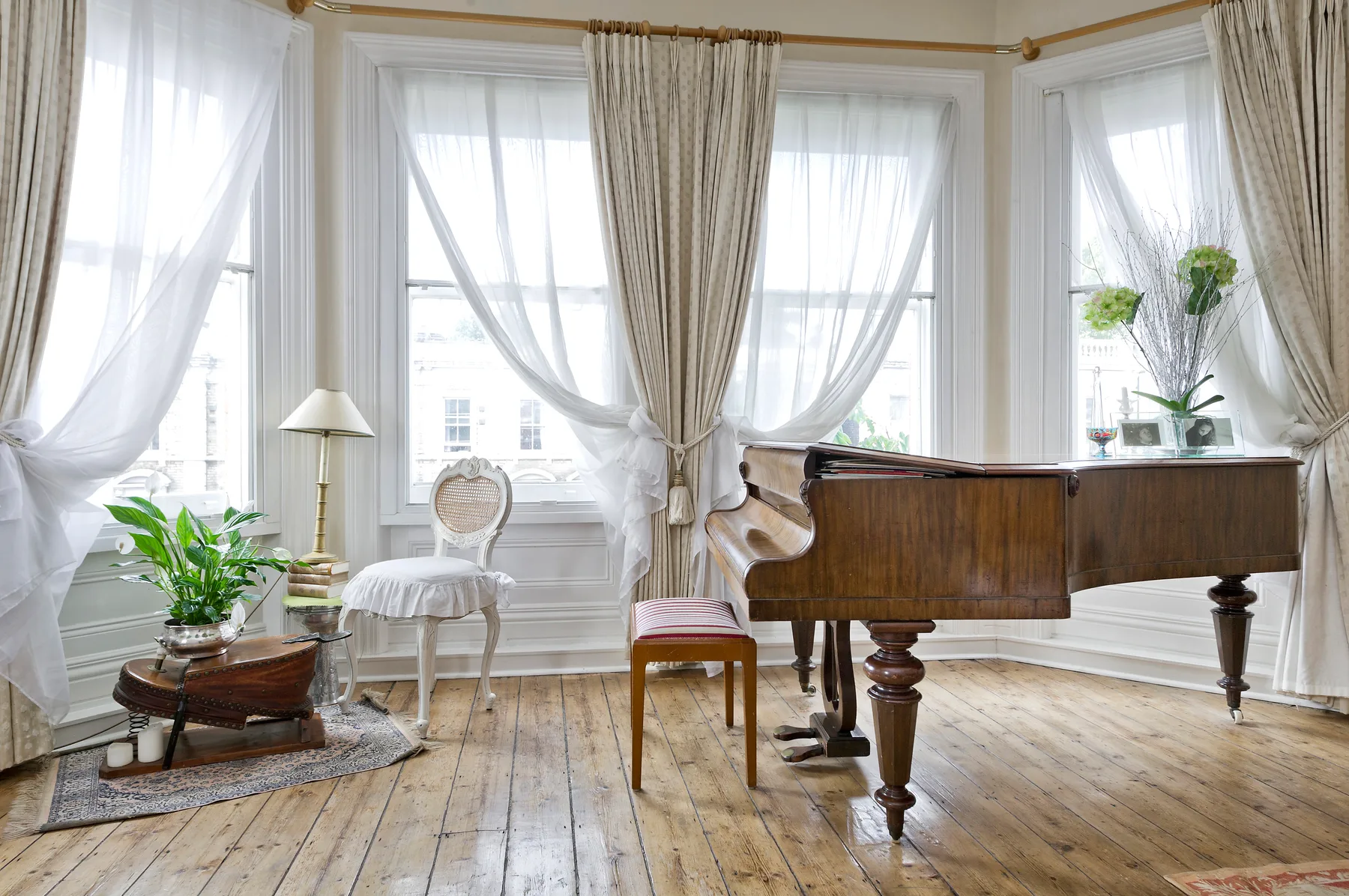 Un piano está en una habitación luminosa con ventanas altas y cortinas vaporosas.