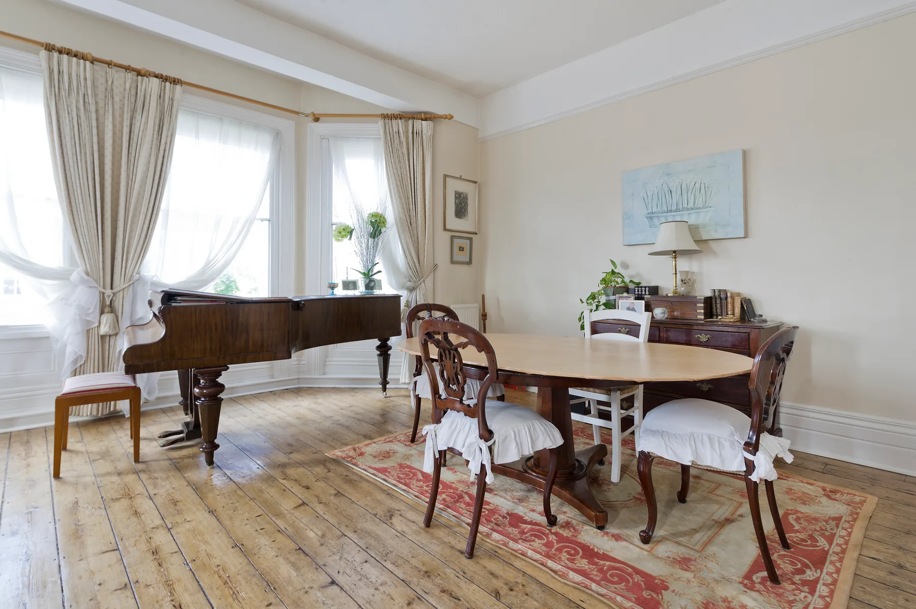 Un comedor luminoso con una mesa de madera y un piano junto a las ventanas.
