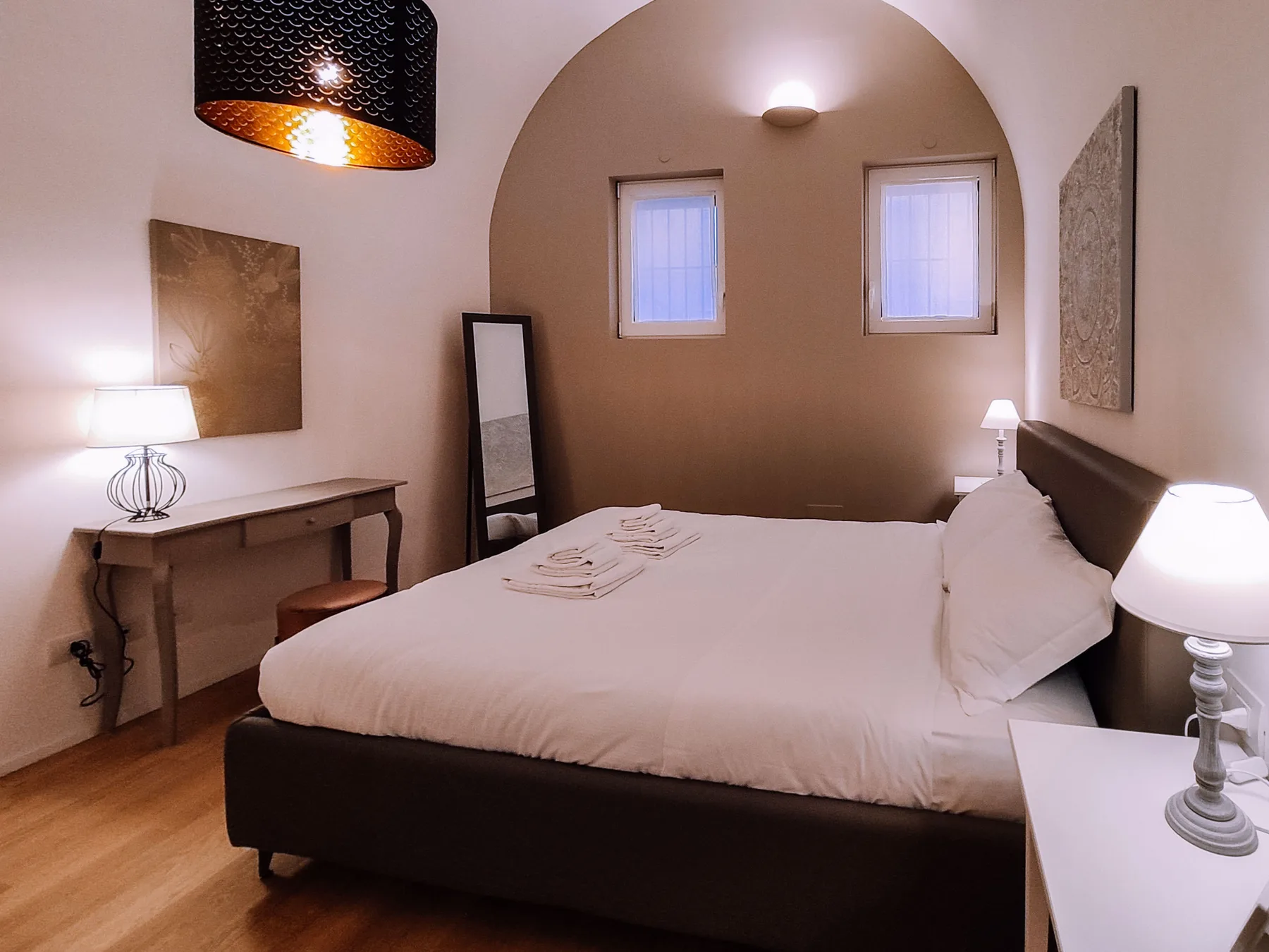 A bedroom with a neatly made bed and two windows beneath an arched alcove.