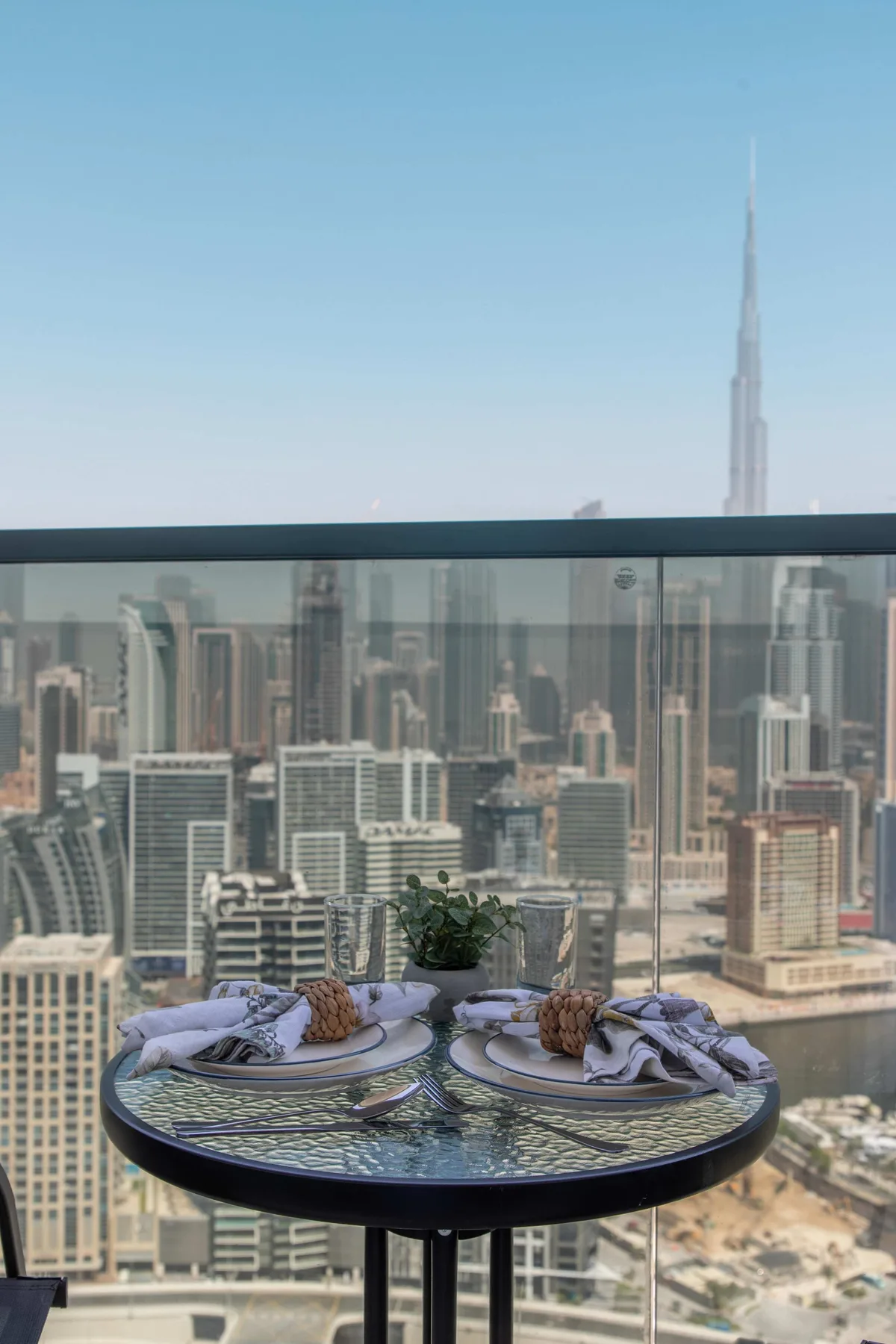 Una mesa de comedor en una azotea está puesta con platos y servilletas frente al horizonte urbano.