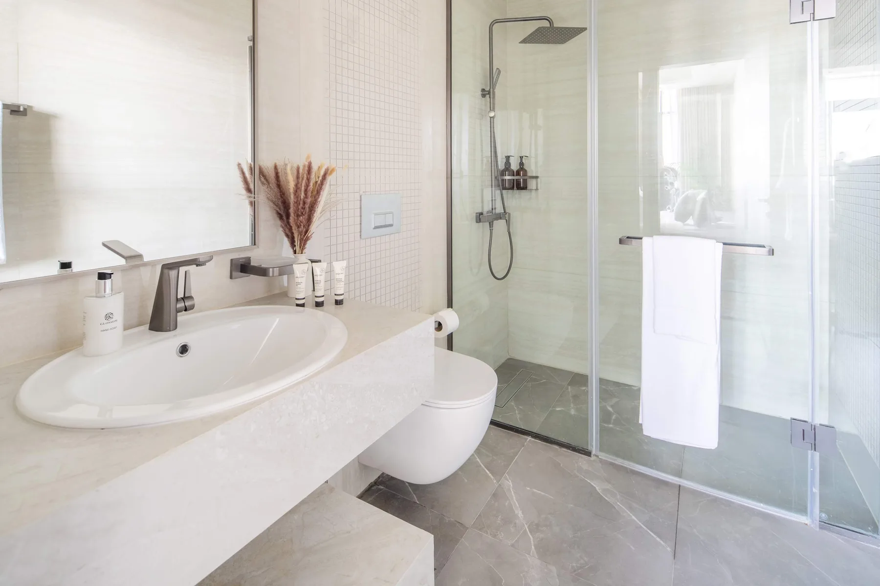 Un baño luminoso con lavabo, inodoro y ducha de vidrio.