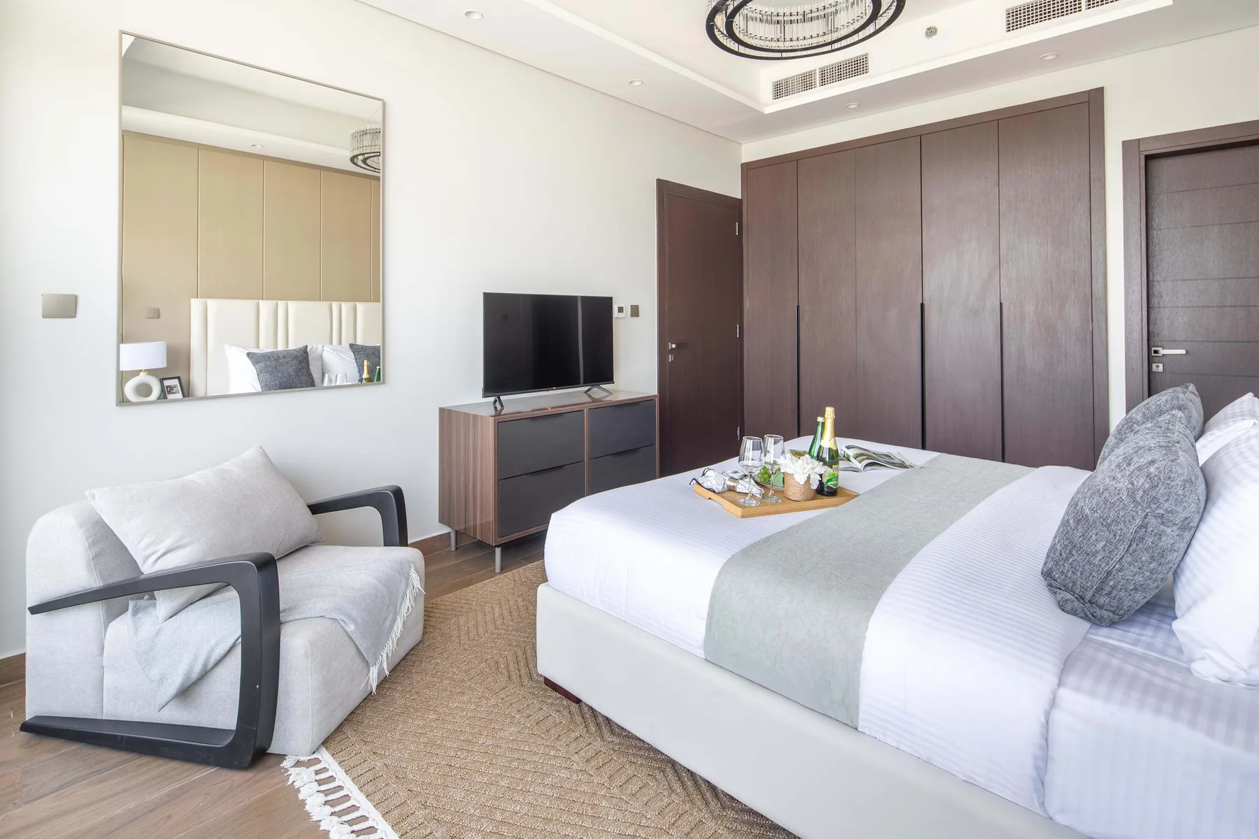 Un dormitorio luminoso con una cama grande, un sillón y un televisor.