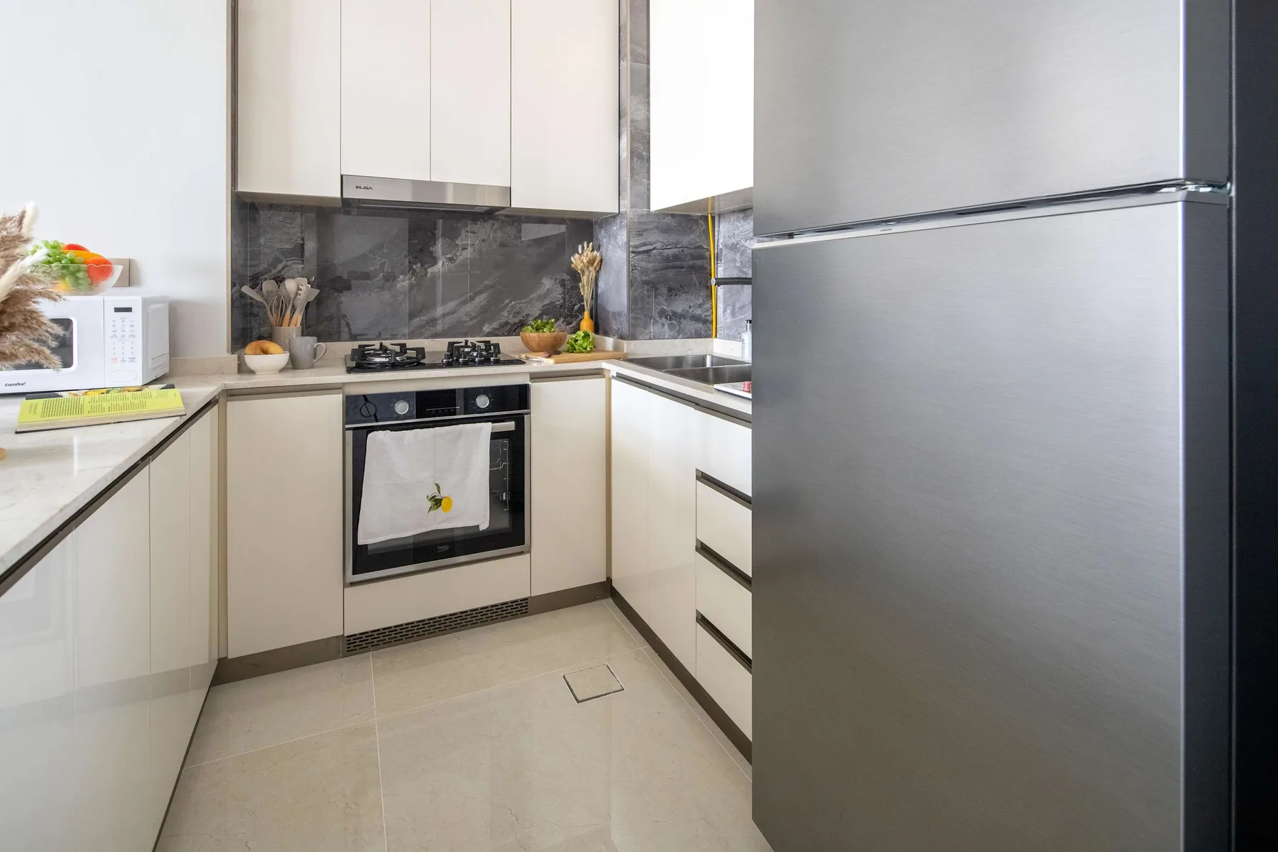 Una cocina moderna con gabinetes claros, horno empotrado y refrigerador grande.