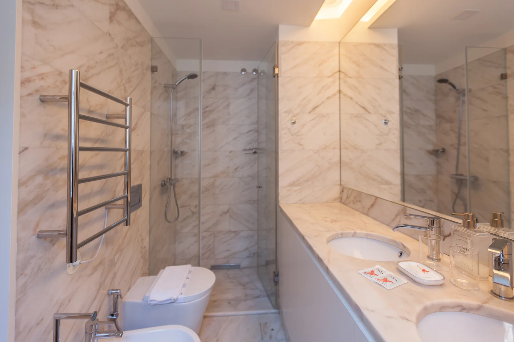 Un baño de mármol con ducha de cristal, bañera y lavabo.