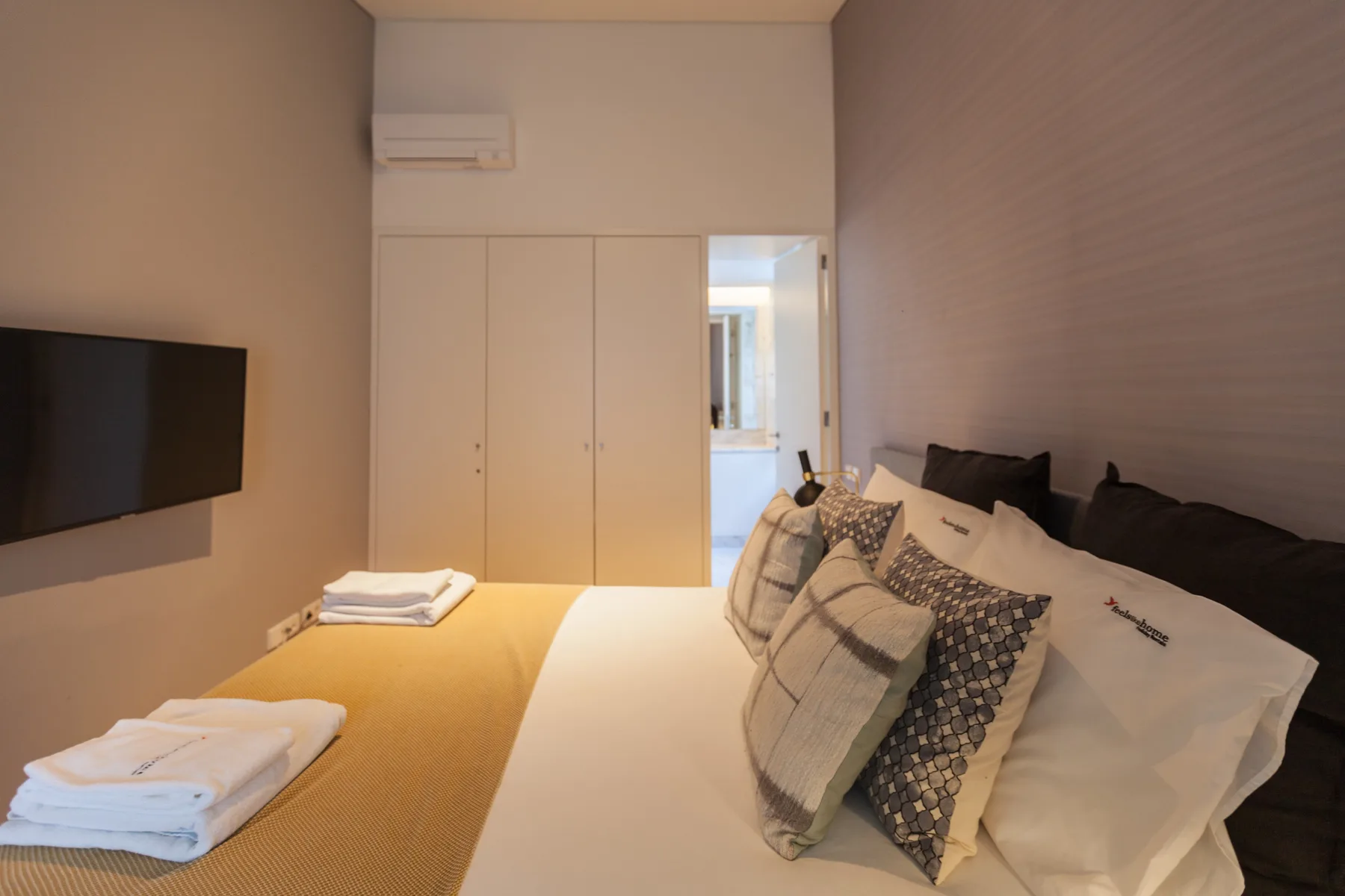 Un dormitorio con una cama, almohadas y un televisor montado en la pared.