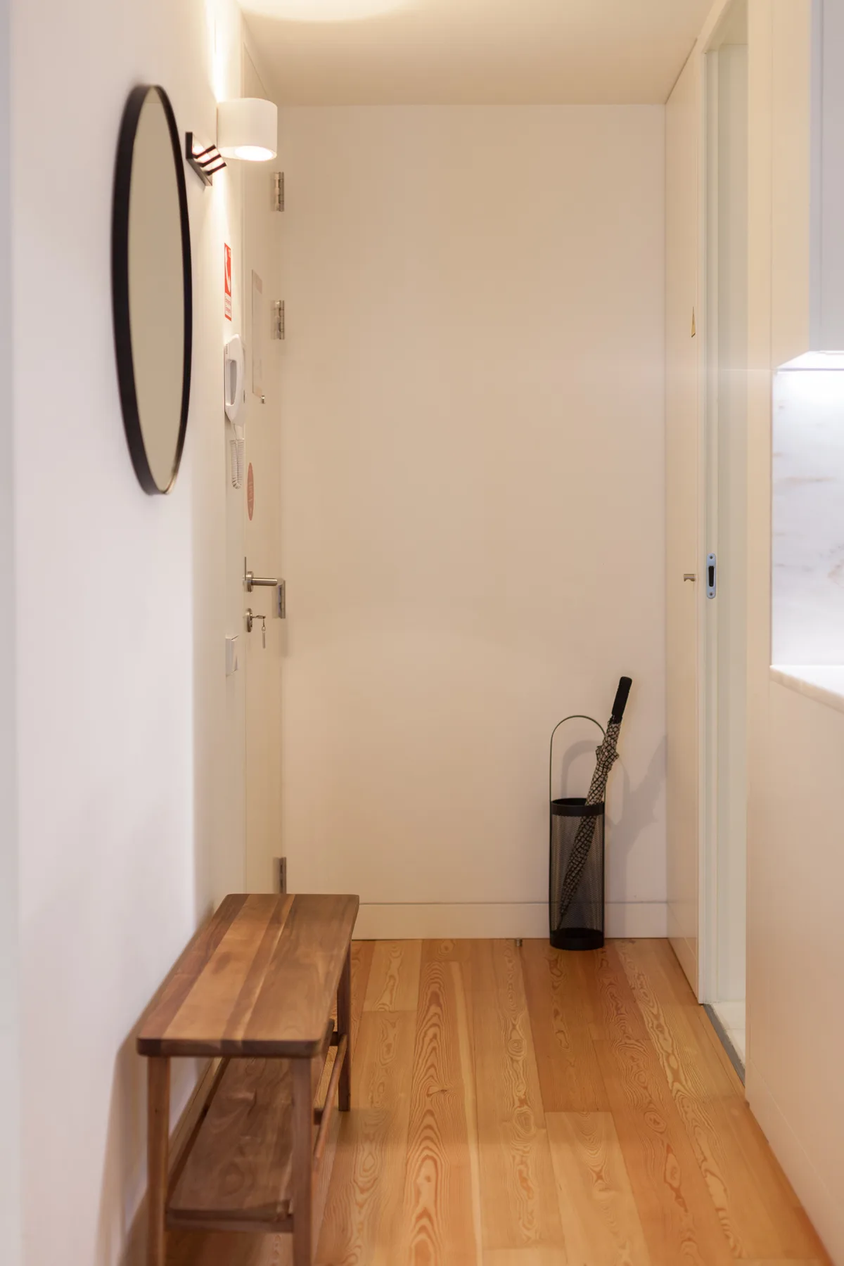 Un pasillo estrecho con suelo de madera y un banco pequeño junto a la puerta.