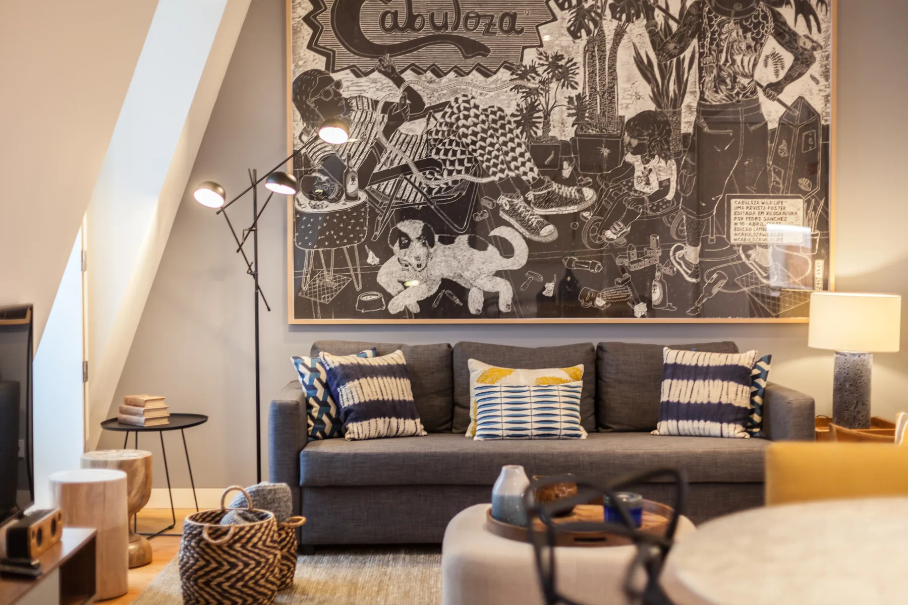 Sala de estar con un sofá gris bajo un gran tapiz ilustrado.