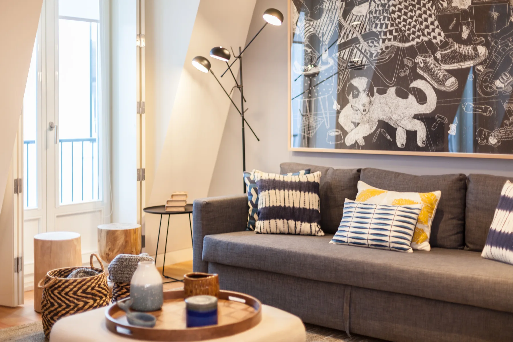 Sala de estar con sofá gris, cojines estampados y una lámpara de pie.