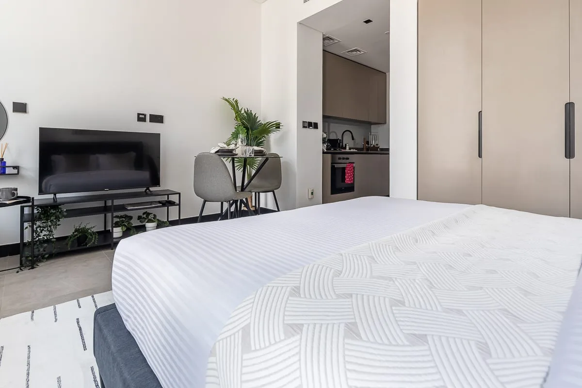 Un dormitorio con una cama bien hecha, un televisor y una pequeña zona de comedor.
