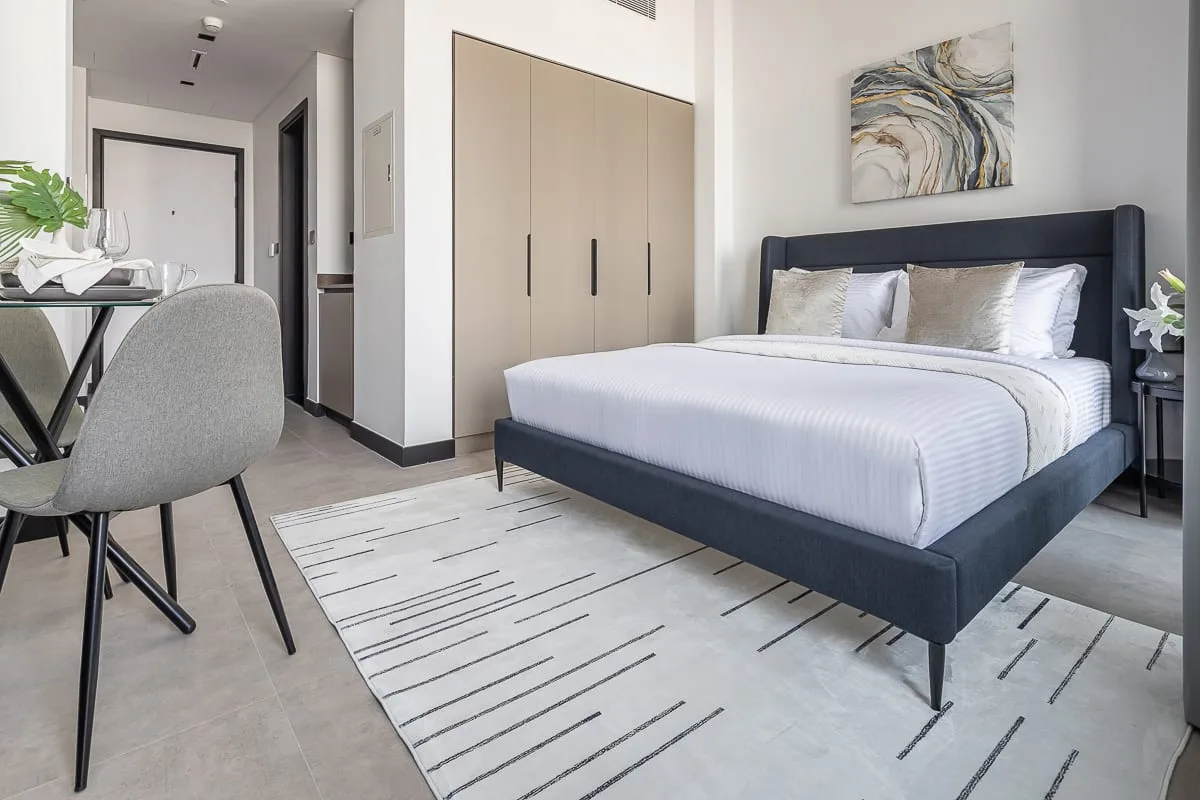 Un dormitorio con una cama, un escritorio y una alfombra clara.