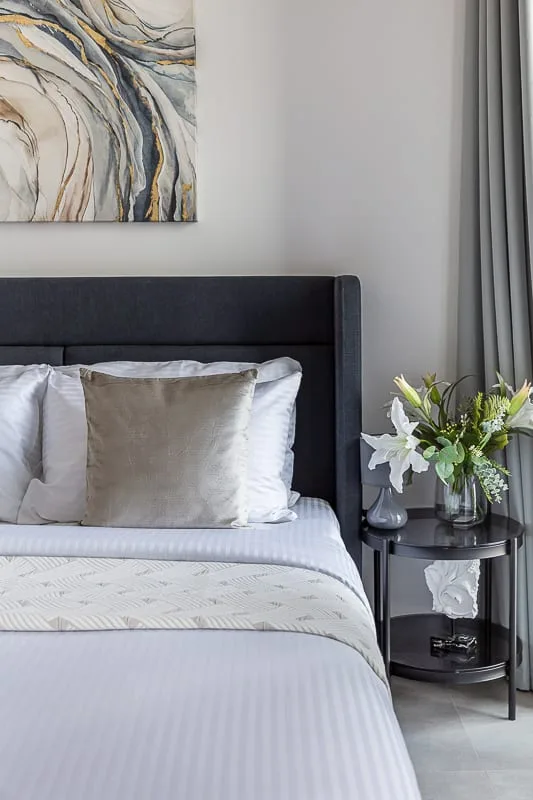 Un dormitorio con una cama bien hecha junto a una mesita con flores.