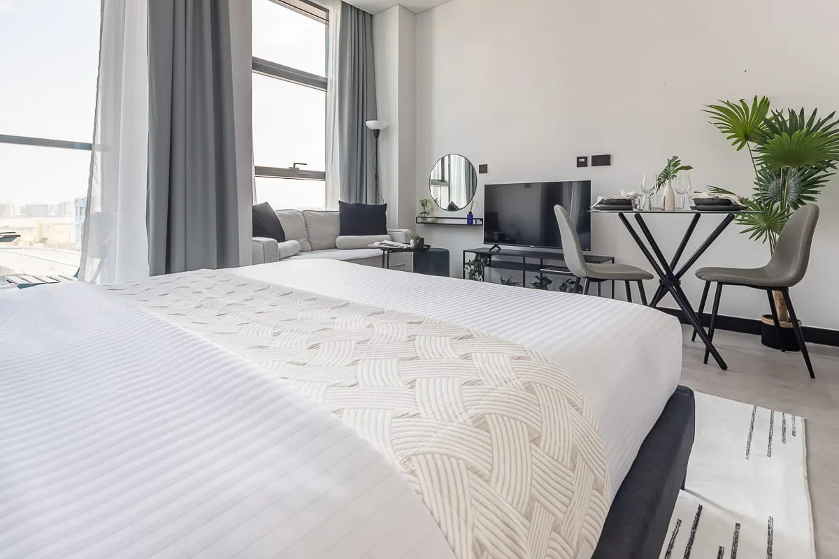 Un dormitorio luminoso con una cama tendida y un escritorio junto a la ventana.