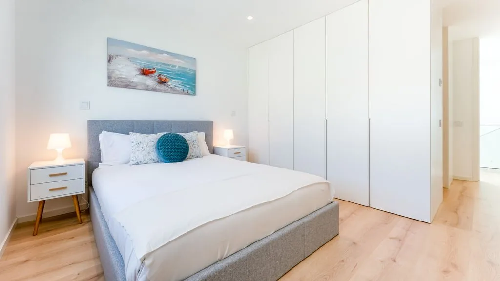 A bright bedroom with a neatly made bed and white built-in wardrobes.