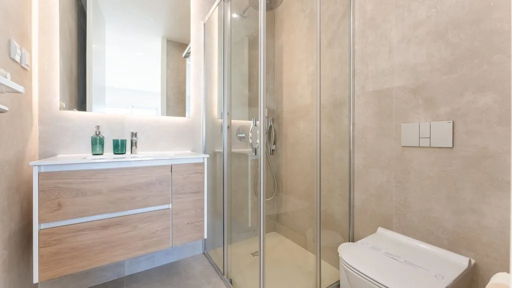 A bathroom with a vanity, mirror, glass shower, and toilet.