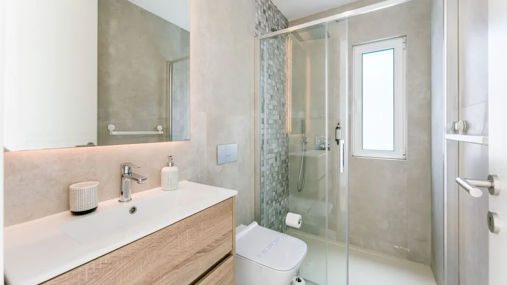 A bright bathroom with a sink, mirror, and glass shower.