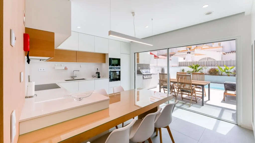 A bright modern kitchen and dining area opens onto a patio beside a pool.