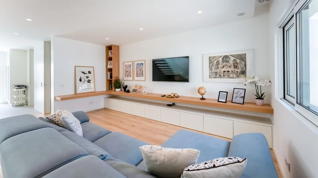 A bright living room with blue seating, a wall-mounted television, and framed artwork.
