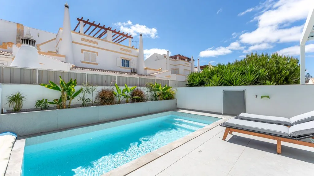 An outdoor swimming pool beside a paved deck and cushioned loungers.