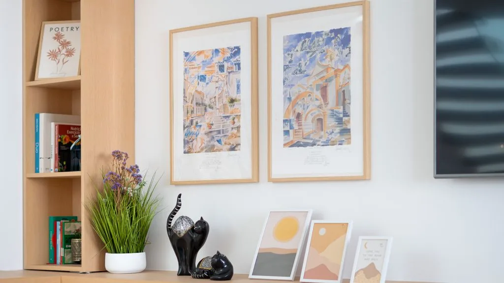 A bright living area features framed artwork, books, and decorative objects on a shelf.