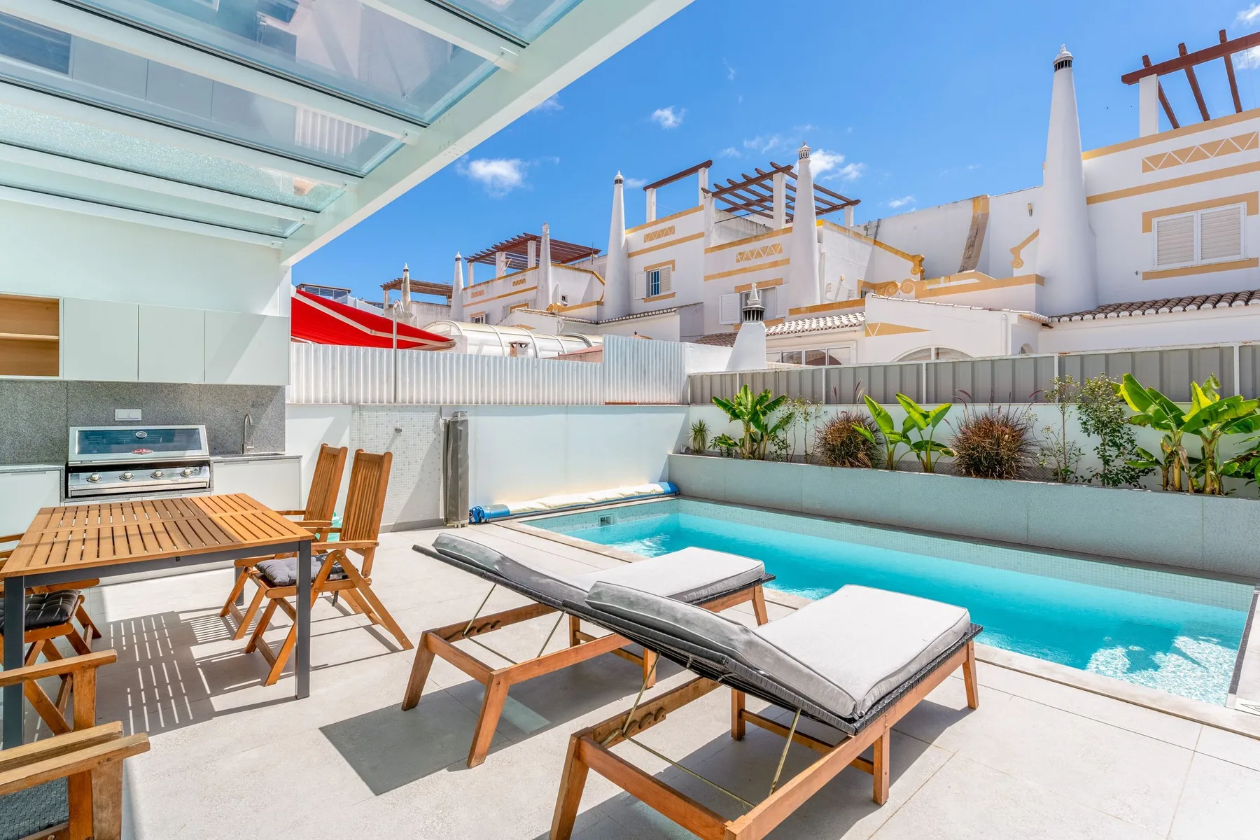 A sunlit patio with a swimming pool, lounge seating, and an outdoor dining table.