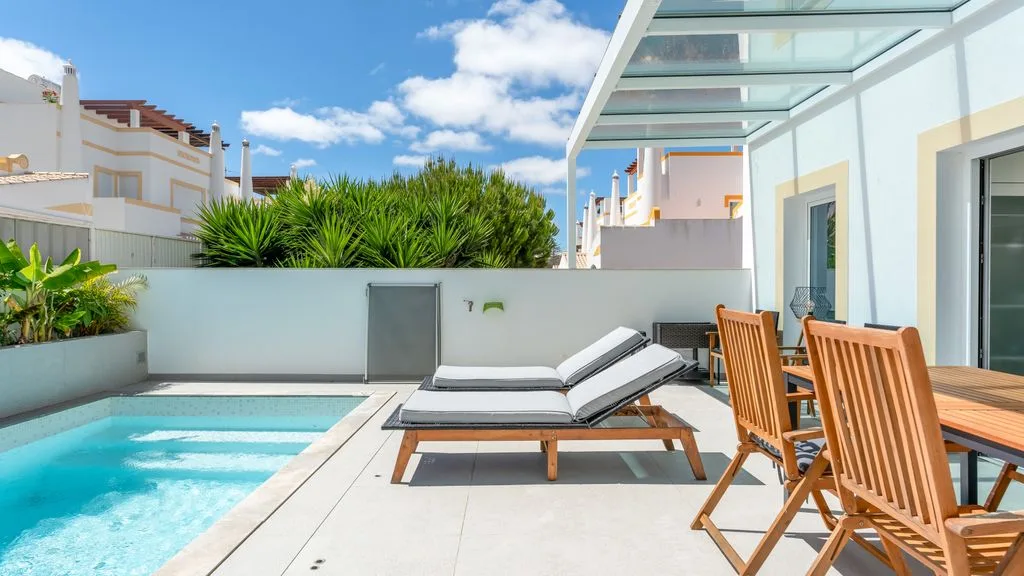A sunny patio with a swimming pool, lounge seating, and an outdoor dining area.