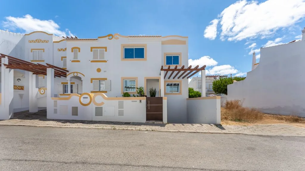 A white two-story house with a walled front patio and pergola.