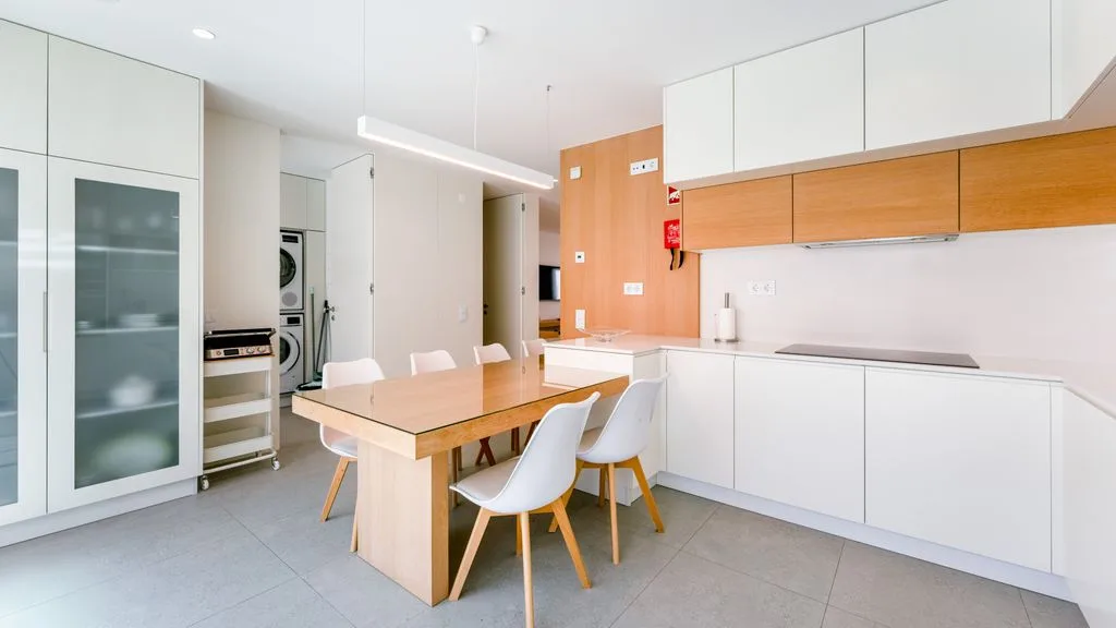 A modern kitchen and dining area with a wooden table and white cabinetry.