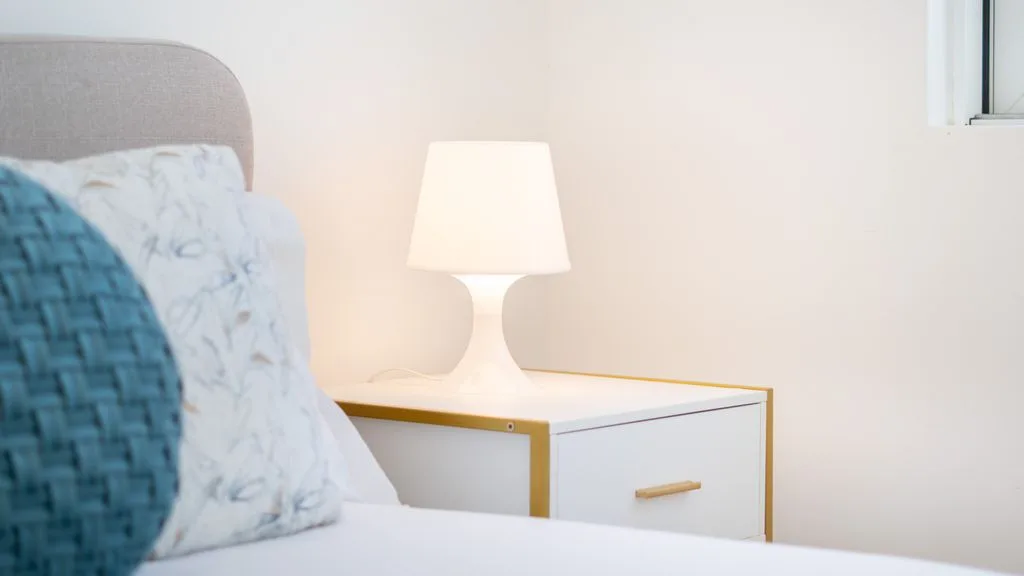 A bedroom with a bedside table and illuminated lamp beside the bed.