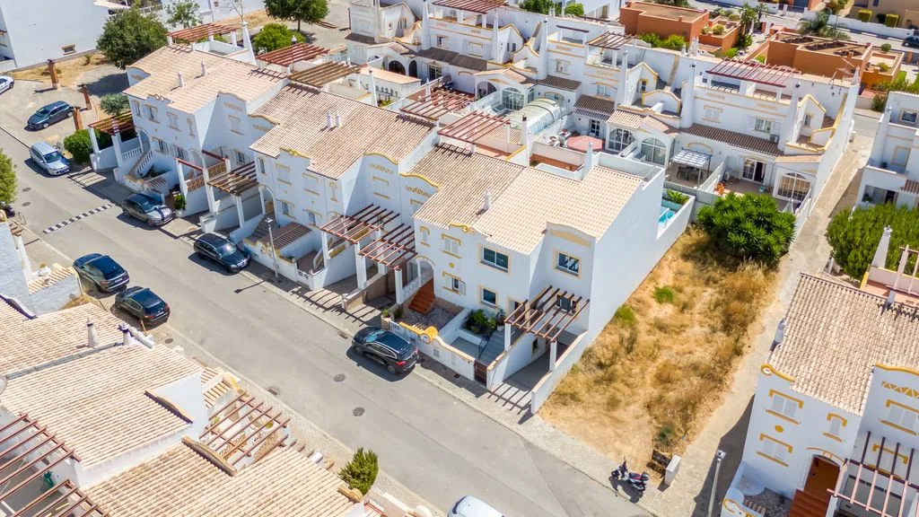 An aerial view of a residential street lined with white houses and parked cars.