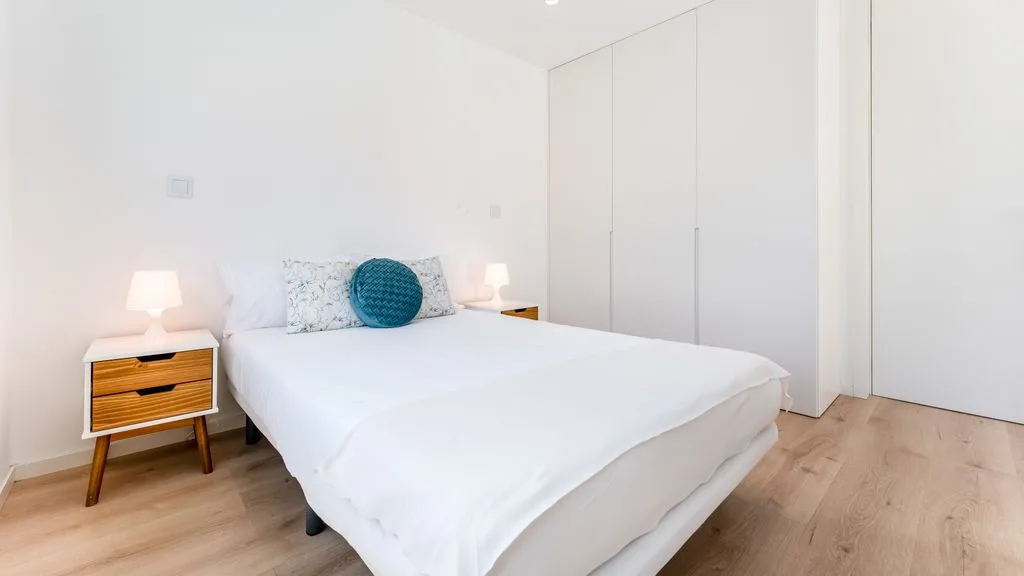 A bright bedroom with a neatly made bed and wooden bedside tables.