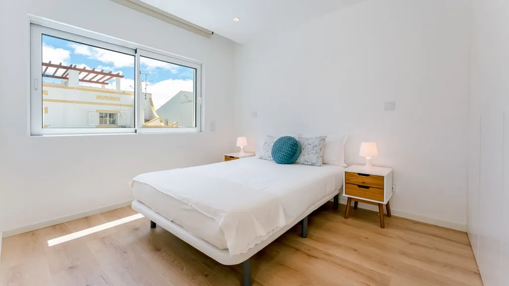 A bright bedroom with a bed beneath a large window.