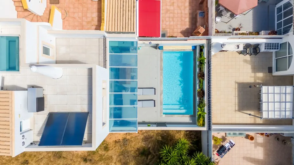 An aerial view shows a rectangular swimming pool beside a paved patio.