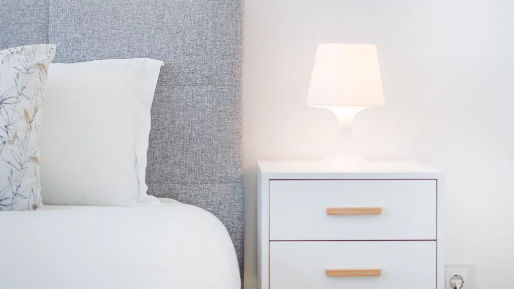A bedroom corner with a bed beside a lit bedside lamp.