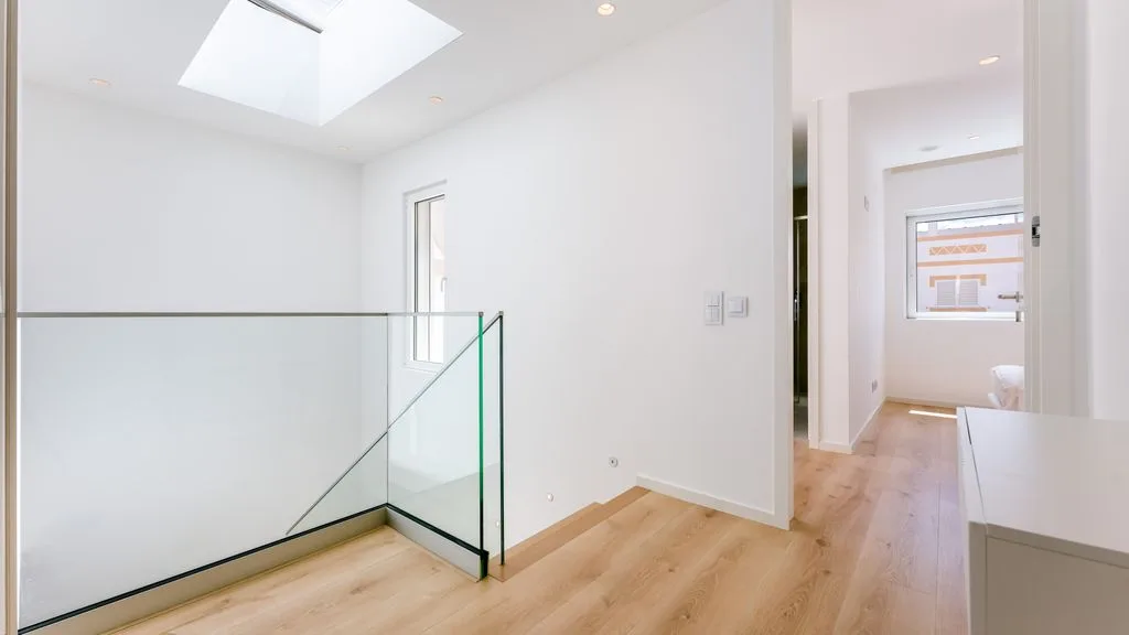 A bright upstairs hallway with light wood flooring and a glass railing.