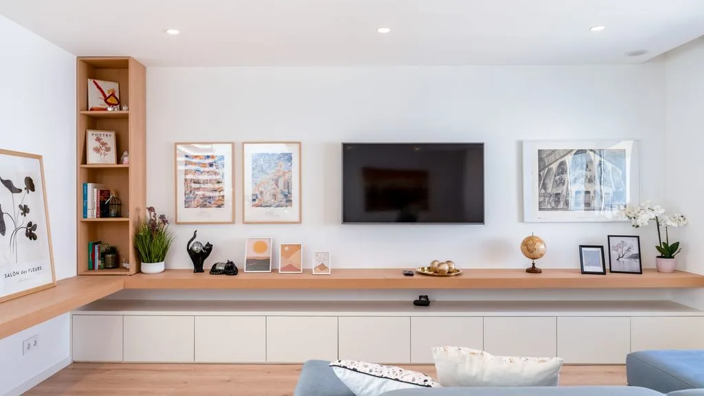 A bright living room with a wall-mounted television above built-in cabinets.
