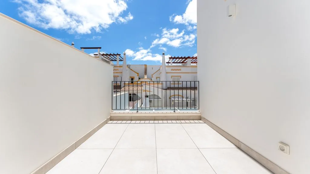 A sunlit outdoor terrace with pale tiled flooring and a black railing.
